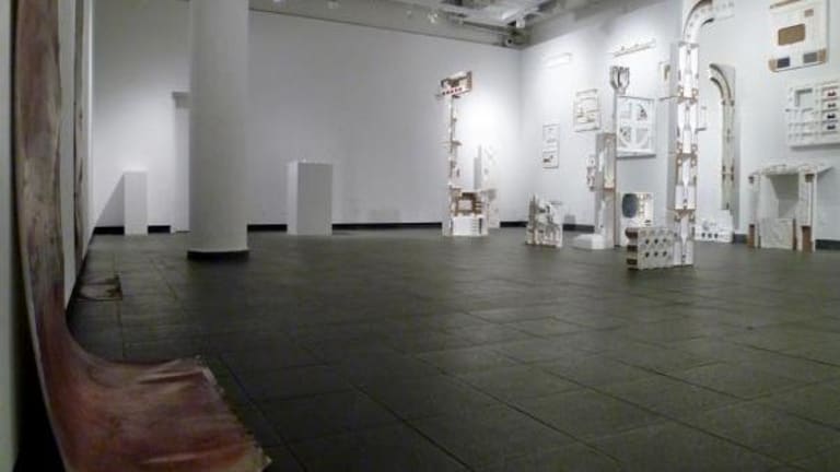 A canvas is draping on the floor of a gallery. There is a sculptural installation in a gallery.