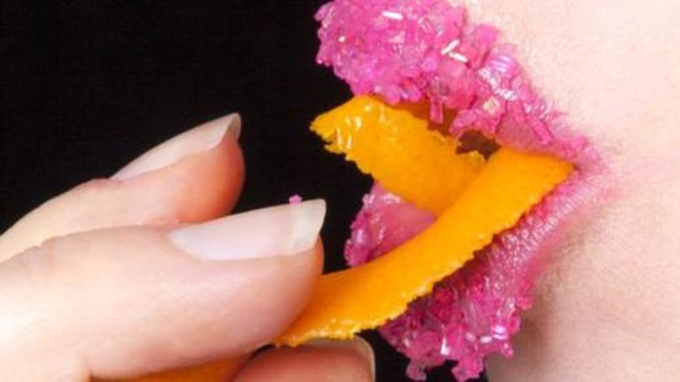 A woman with sprinkles on her lips. She is holding something yellow-orange to her lips.