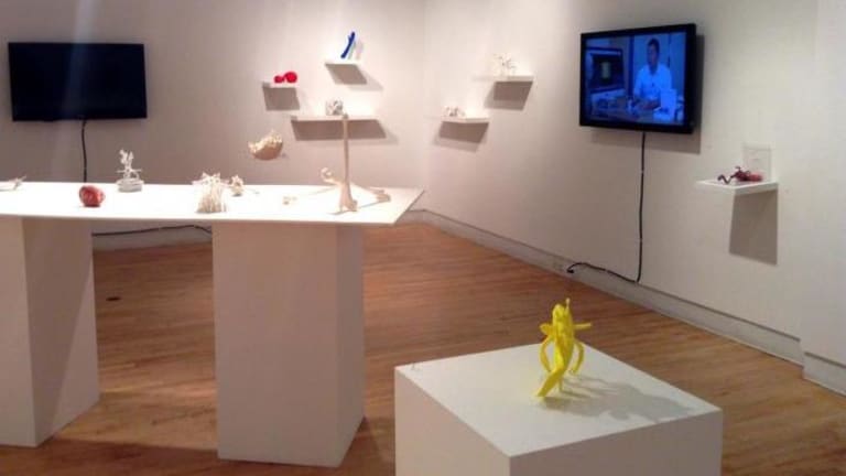 A collection of small sculptures in an art gallery.  A TV screen is mounted to the wall.