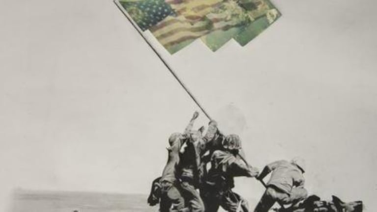 A group of four soldiers hoisting an american flag which is made up of colored images on a rock near the water