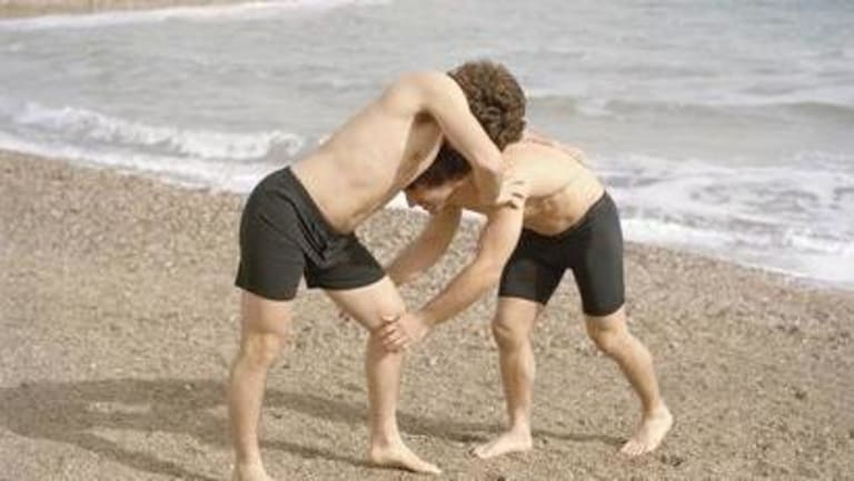 Two guys wresting at the beach.