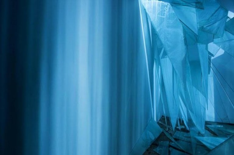 A blue photo of an art installation featuring curtains and lighting