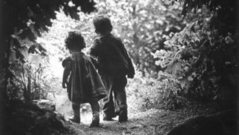 Black and white photograph of two small children walking out of a wooded area.