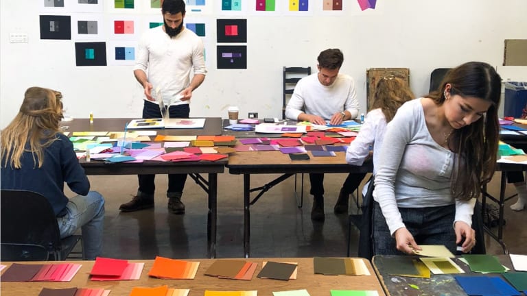 Students in a classroom work on color theory exercises, using sheets of colored paper.