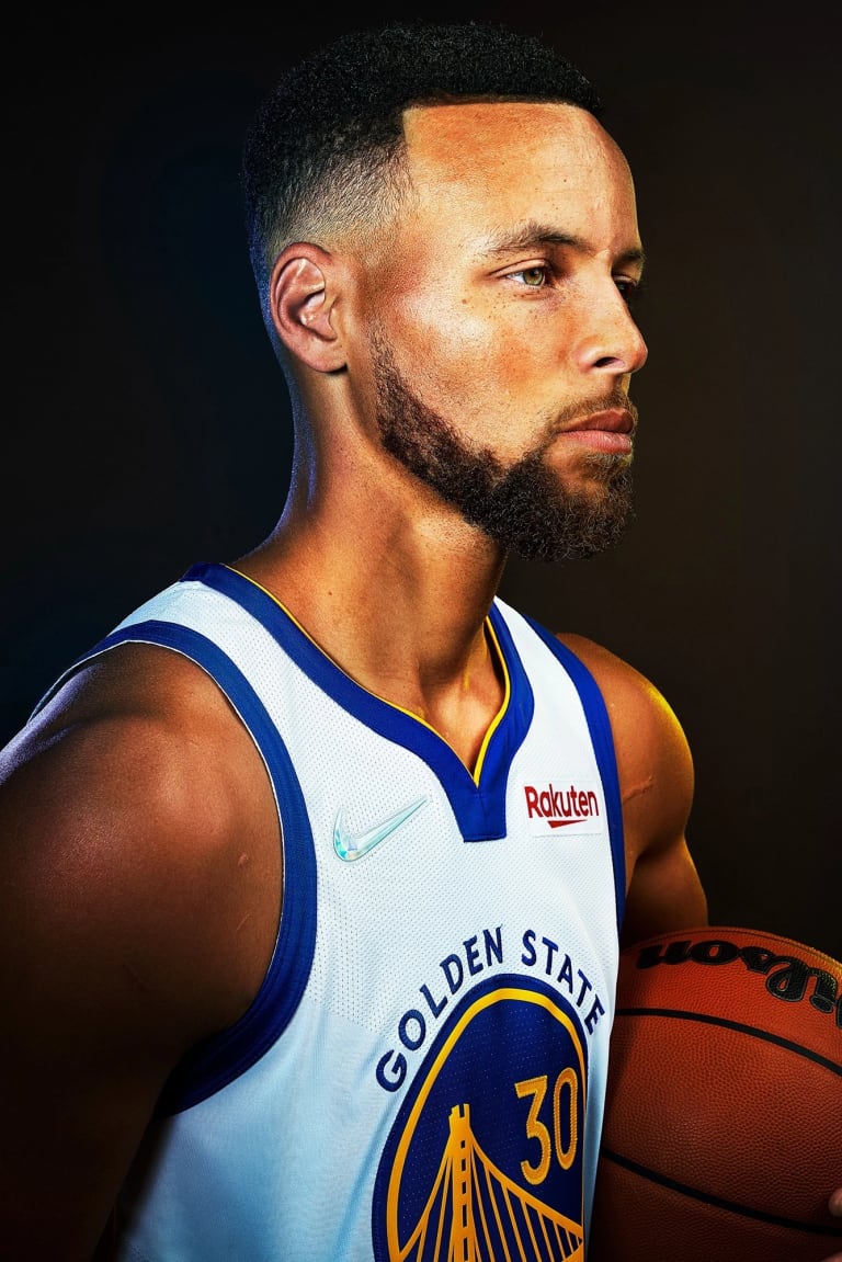 A studio portrait of basketball player Steph Curry. He is holding a basketball and facing the right of the frame.