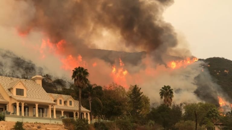 A wildfire spreads in the forest behind a beautiful home in California.