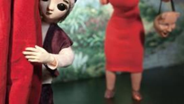 A doll peaking from behind a red curtain with another doll in a red dress behind her holding a mask.