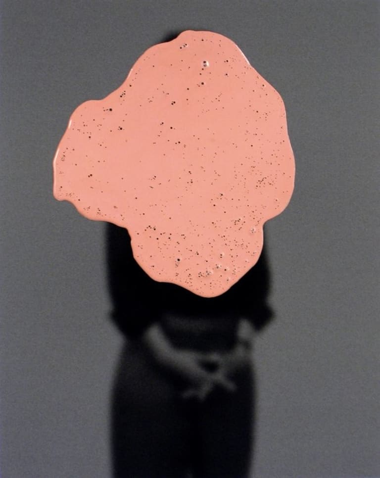 A liquid pink substance with bubbles covering the a silhouetted image.  The background is a grainy gray and the silhouetted image is black.