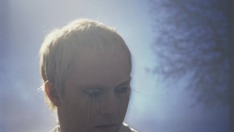 A person, from shoulders up, with short blonde hair and dramatically long blonde eyelashes looks downward