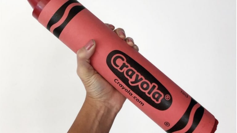 a hand holding up an oversized red crayola crayon