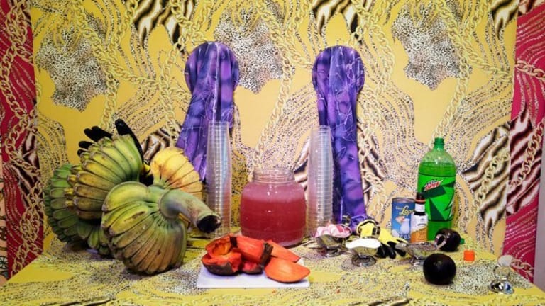A table with various items, some edible some non edible, surrounded by colorful fabric, with two empty arm holes in walls.