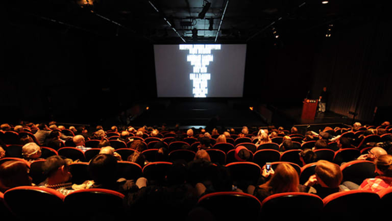 Inside of a movie theater, the audience watches credits roll.