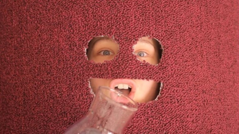 A person making an expression behind a red wall with a face.