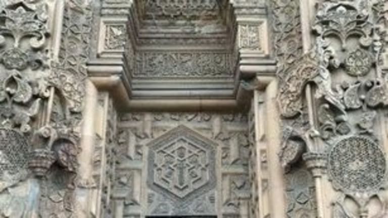 Building entrance surrounded by ornate carvings. The doorway is covered with a black gate.