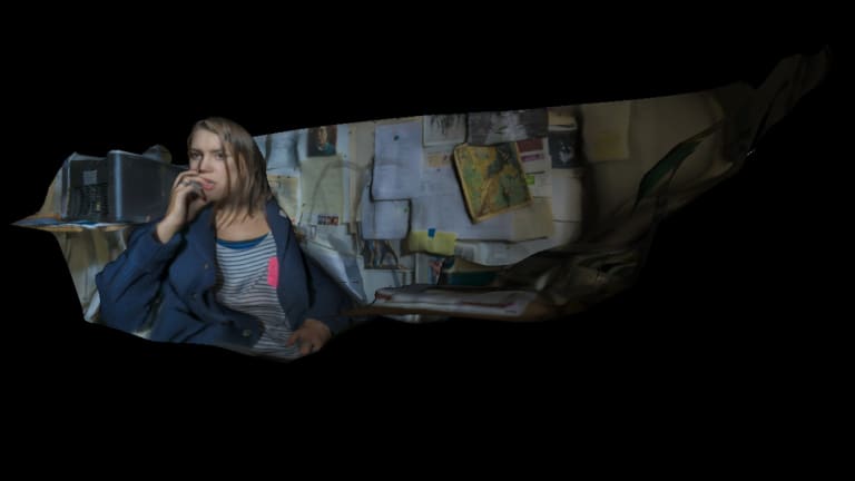 a photograph of a girl sitting at a desk, biting her nail in thought. it looks like the photo has been cut around the outline of the girl and the desk, and is on a black background