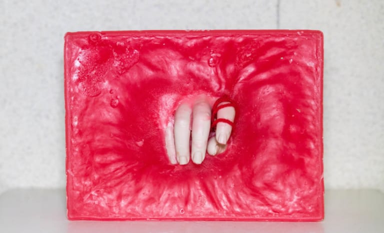 A hand reaches through a hole in a deep pink wall