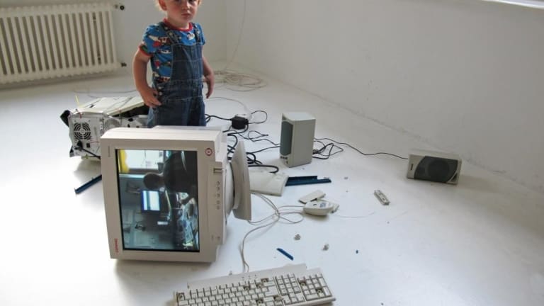 A small child is staning between the ruined computer and is alone