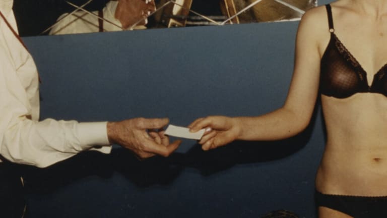 a woman in her underwear hands a man in a white button down a piece of paper