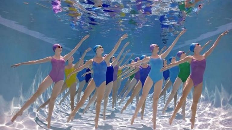 Female synchronized swim team posing under water.