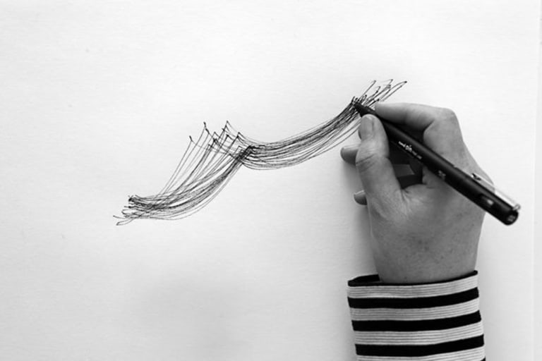 Woman's hand drawing on white paper with a black pen. The photo is incomplete.