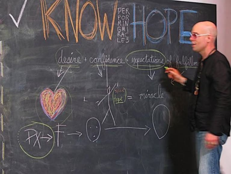 A man at a chalk board in the midst of circling a word. The chalk board has words and diagrams in multiple colors.