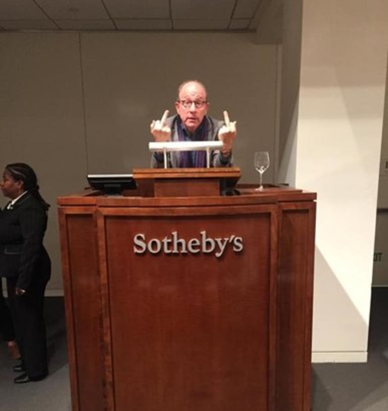 Man standing behind a Sotheby's lectern giving the middle finger