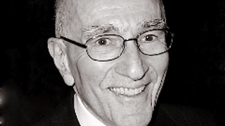 A smiling older man wearing glasses, a black suit and a tie.