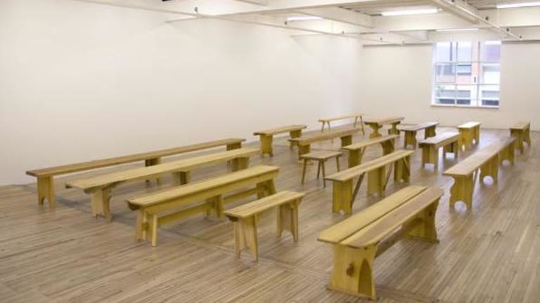 A wide spacious white room with a wooden floor accompanied by 17 different wooden benches each being different sizes and different models in structure.