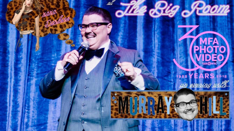 photo of Murray Hill on stage with a microphone in a 3-piece suit, with a bright blue stage curtain backdrop