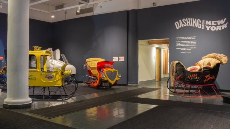 Photograph of front gallery space with multiple designed sleighs and the exhibition title "Dashing Through New York" on the back wall.