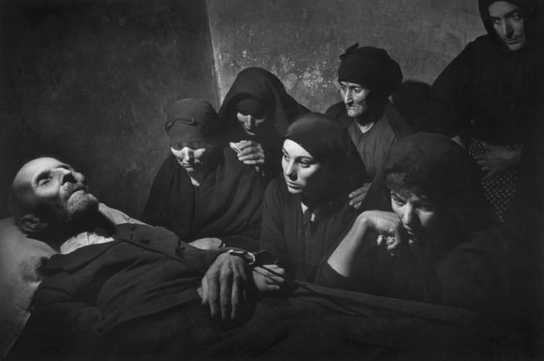 A black and white image of women sitting around a person in a bed.