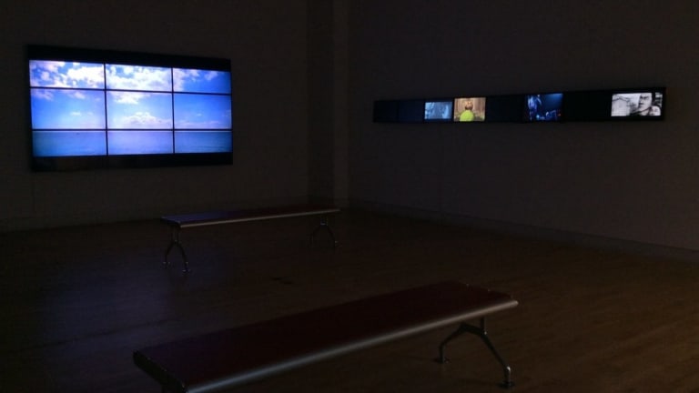 A room with 2 benches and a few tv screens. One is set to look like a window.