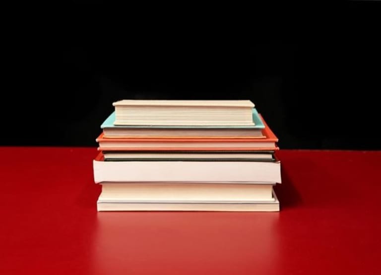 Seven books stacked on top of eachother on a red table.