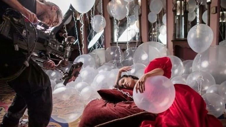 A videographer films a model in a red dress laying on a couch in a room filled with balloons