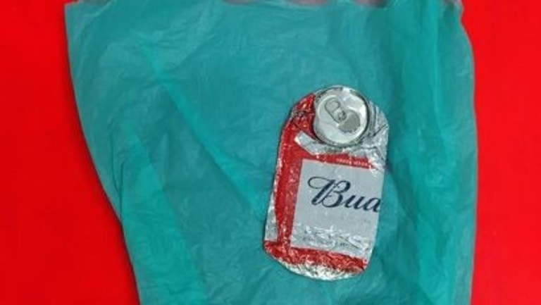 A crushed Budweiser can sits on top of a green plastic bag.