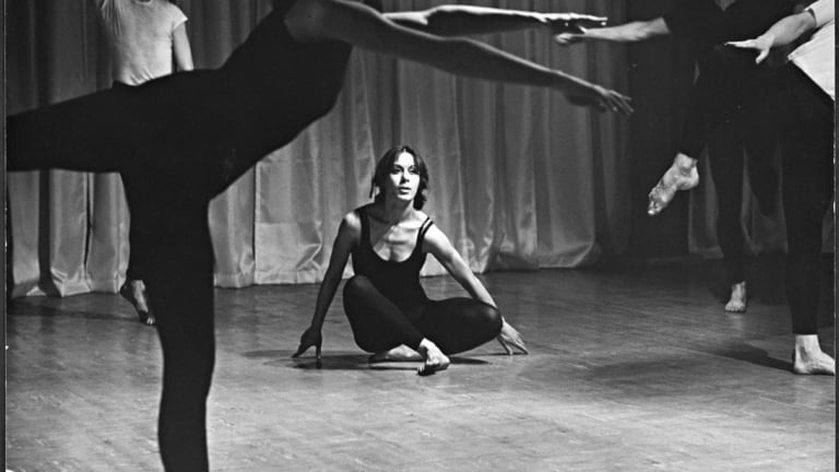 A woman sits on the floor of a dance studio, and in the foreground you can see the bodies of other dancers.