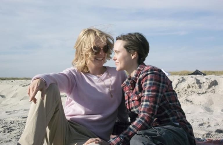 Two women sitting on the beach smiling during the daytim.