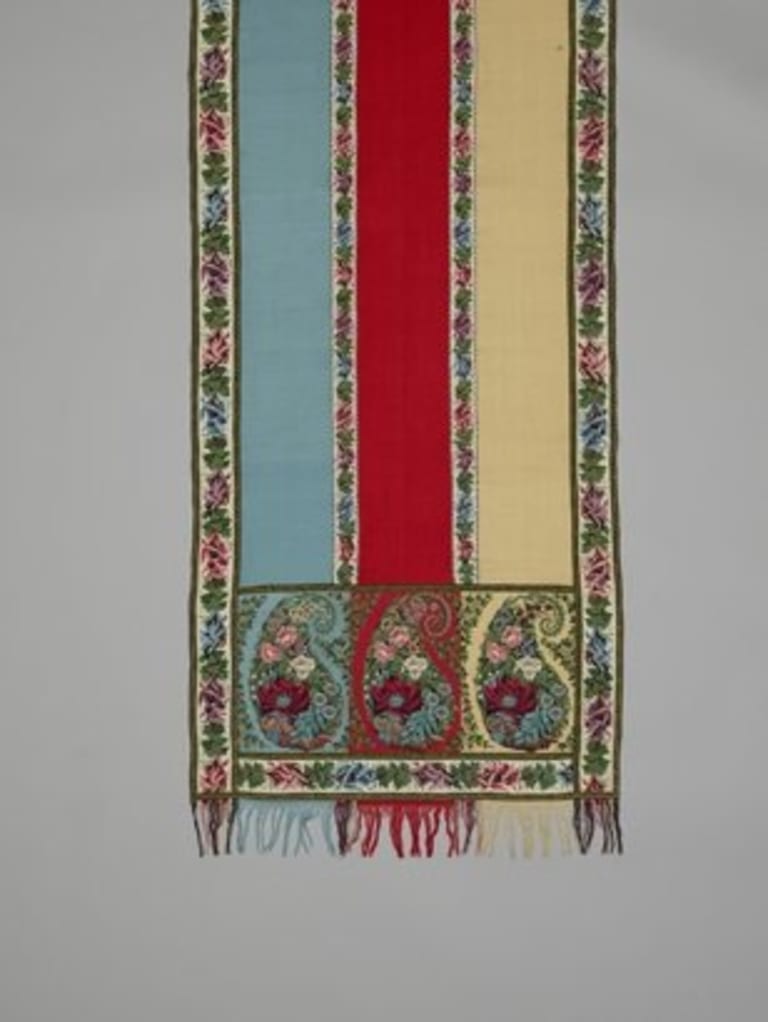 A turquoise, red and yellow rug with flower borders and paisley designs at the end.