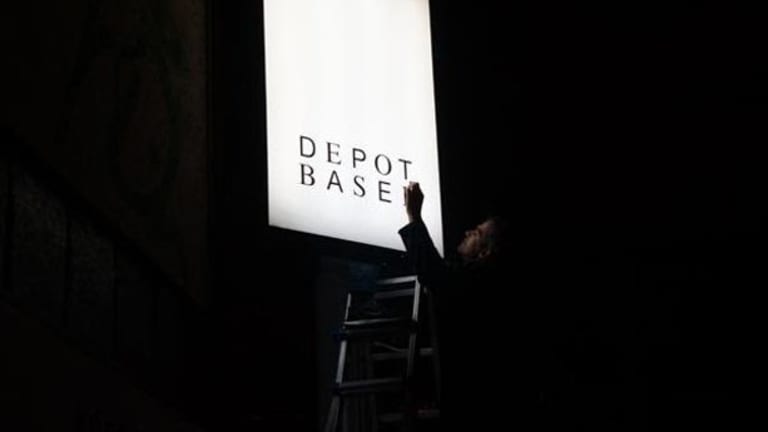 A man on a ladder cleans a back-lit sign at night.