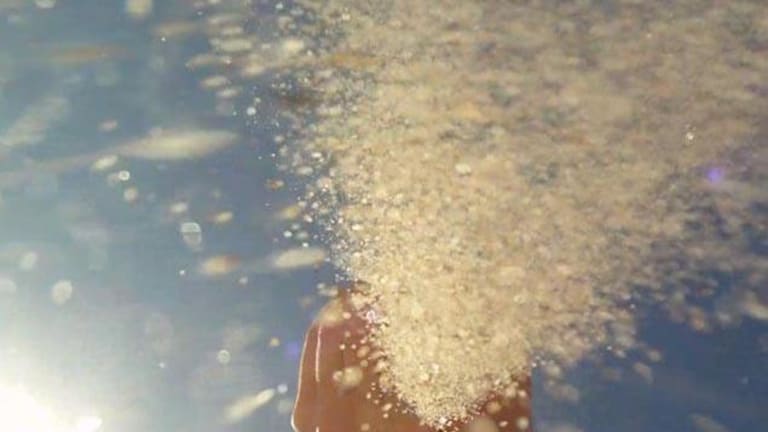 A slow-motion shot of sand blowing from a hand.