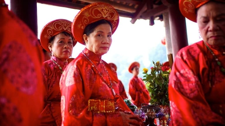 A group of elderly ladies dressed in bright red clothing, 2 of which are looking directly at the camera.