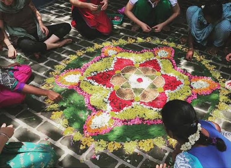 Colorful art created with flowers and leaves. The people creating it are huddled around in a circle.