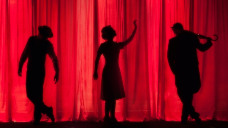 3 silhouettes acting different gestures in front of a red curtain.