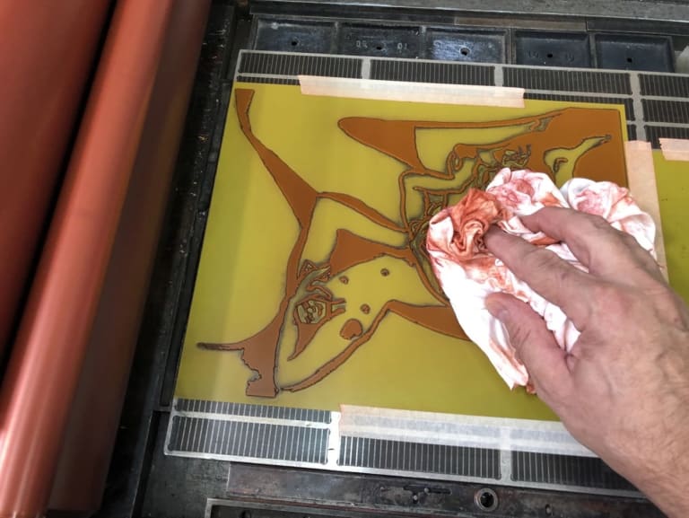 Photo of a hand holding an ink-stained cloth wiping the surface of a letterpress printing plate 