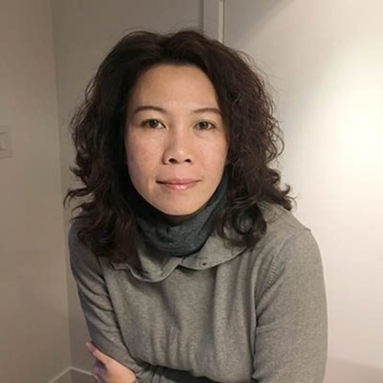 A headshot-style photograph of a person posed in a room with blank walls.