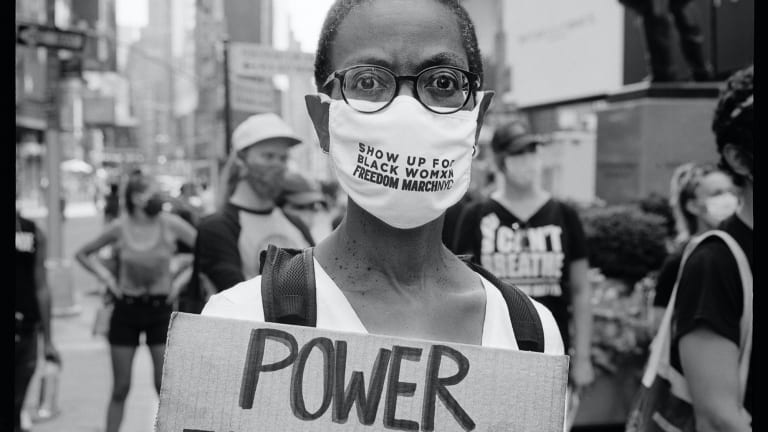 Here is a photo of a protestor in a mask with a handmade sign that reads Power to the People.