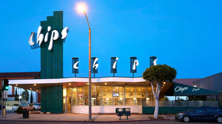 A photograph of the exterior of the Chips Restaurant in Los Angeles, CA, which features a tall, dark green column that bears the name of the restaurant in white letters, and a single story dinning room. 