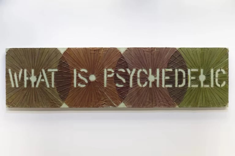 Photo of a painting featuring the phrase "what is psychedelic" hanging on a white gallery wall