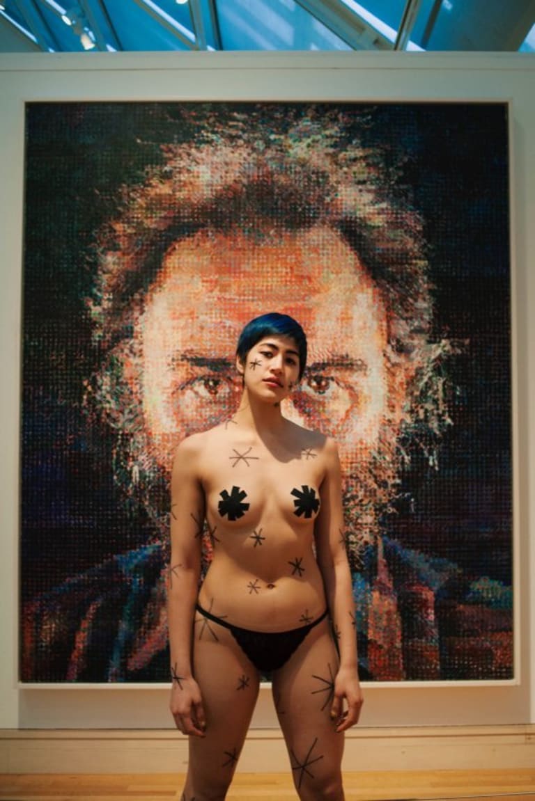Image of an almost-naked person in front of a portrait painting of a man.
