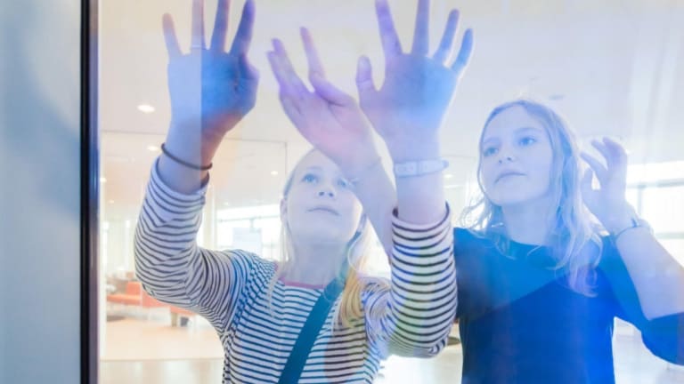 Two kids placing their hands on a glass installation.
